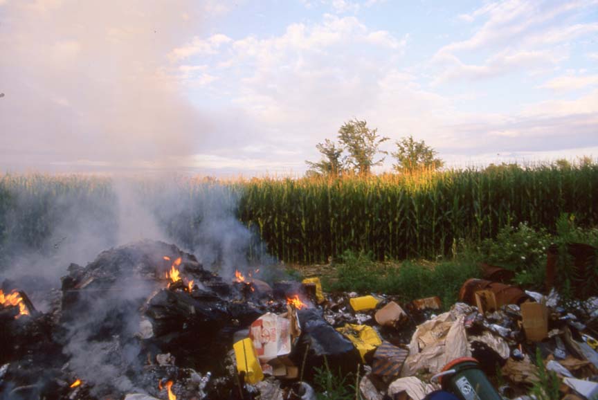 large pile of burning trash beside corn field
